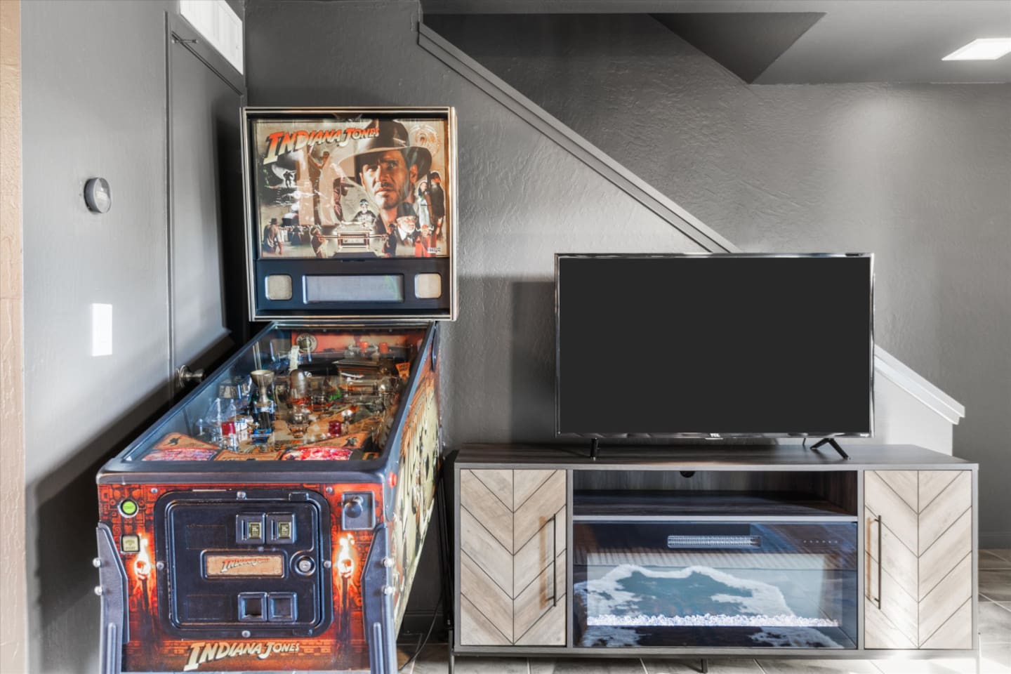 Entertainment corner with Smart TV, fireplace console, and a pinball machine for easy indoor fun.