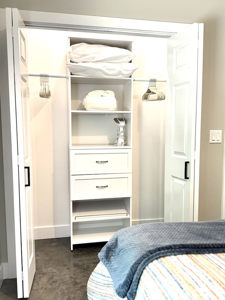Lighted closet with a closet organizer has plenty of space for your hanging items, hangers, extra pillows, and blankets, as well as a steam iron for your clothes.