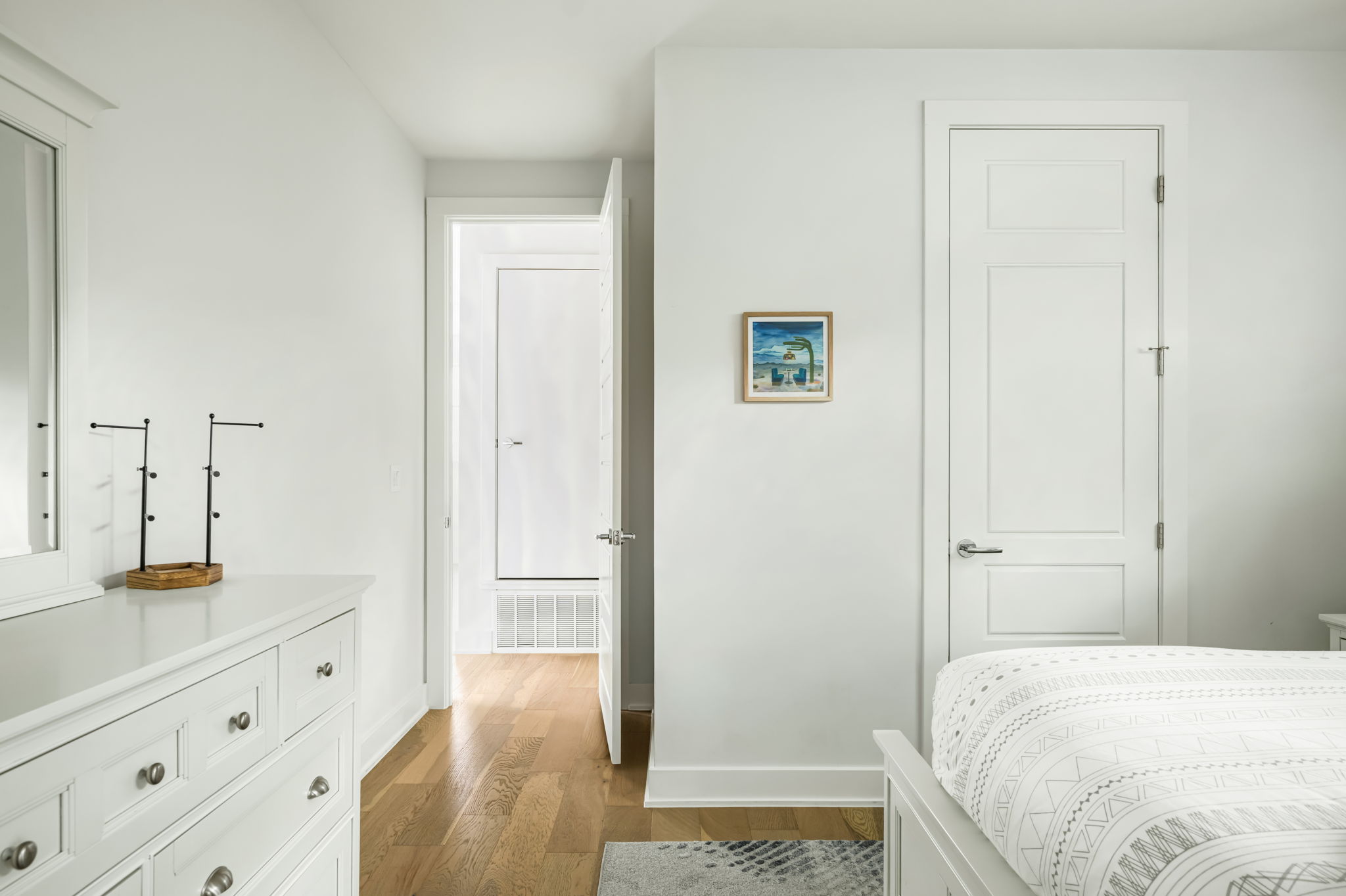 Well-appointed guest room with a stylish dresser, decorative accents, and a bright hallway leading to the rest of the home.