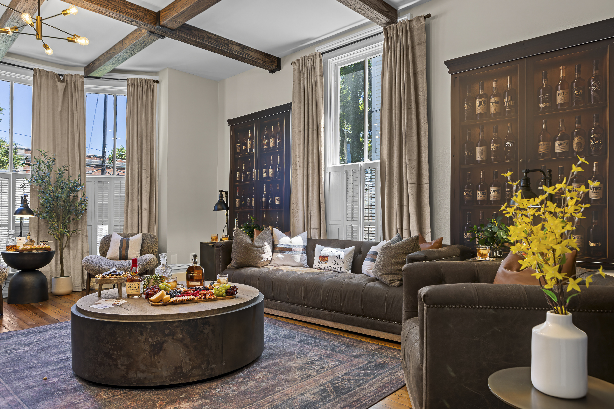 The main living room sets the tone with exposed wood beams, a striking bourbon display cabinet, and comfortable leather seating for the whole group.