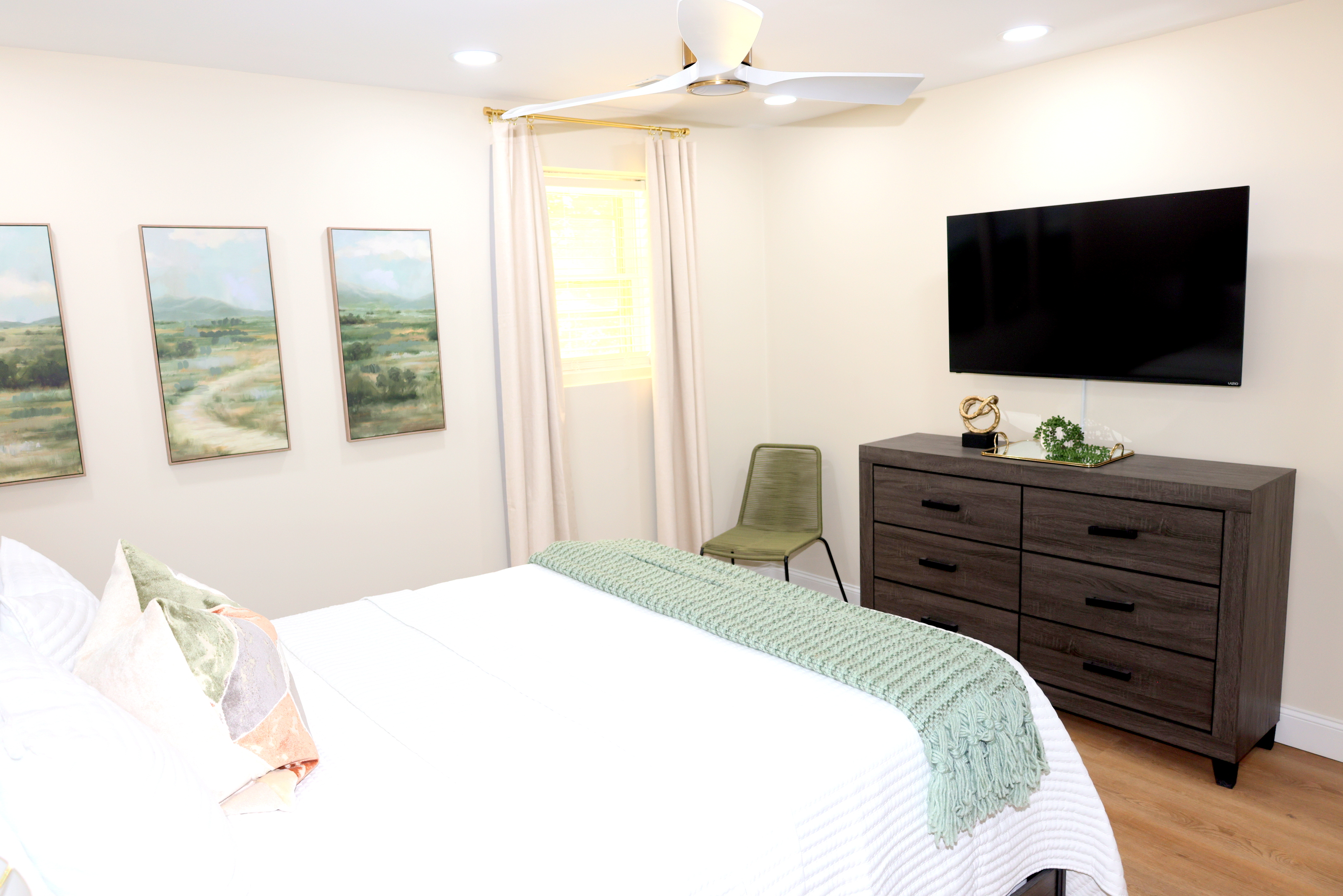 Spacious bedroom with TV, ceiling fan, dresser, and calming neutral décor
