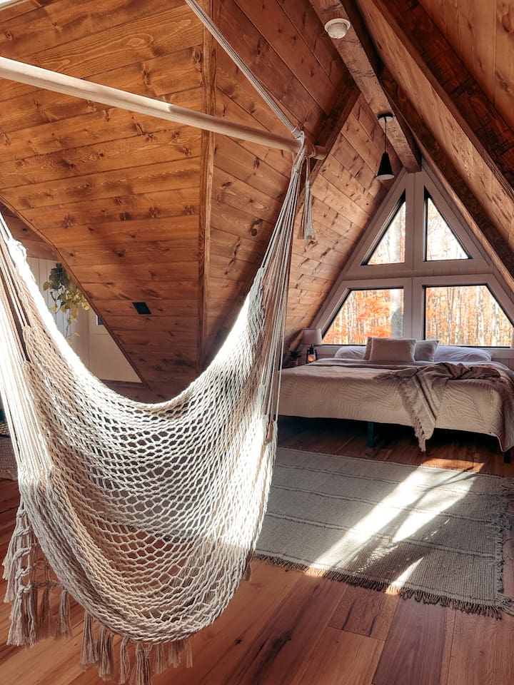 Adding a playful touch, a hammock is ingeniously built into the floor, perfect for lounging and soaking in the serene atmosphere. Nearby, a macrame swing hangs, providing a cozy nook to relax and sway gently while enjoying the tranquil forest view.