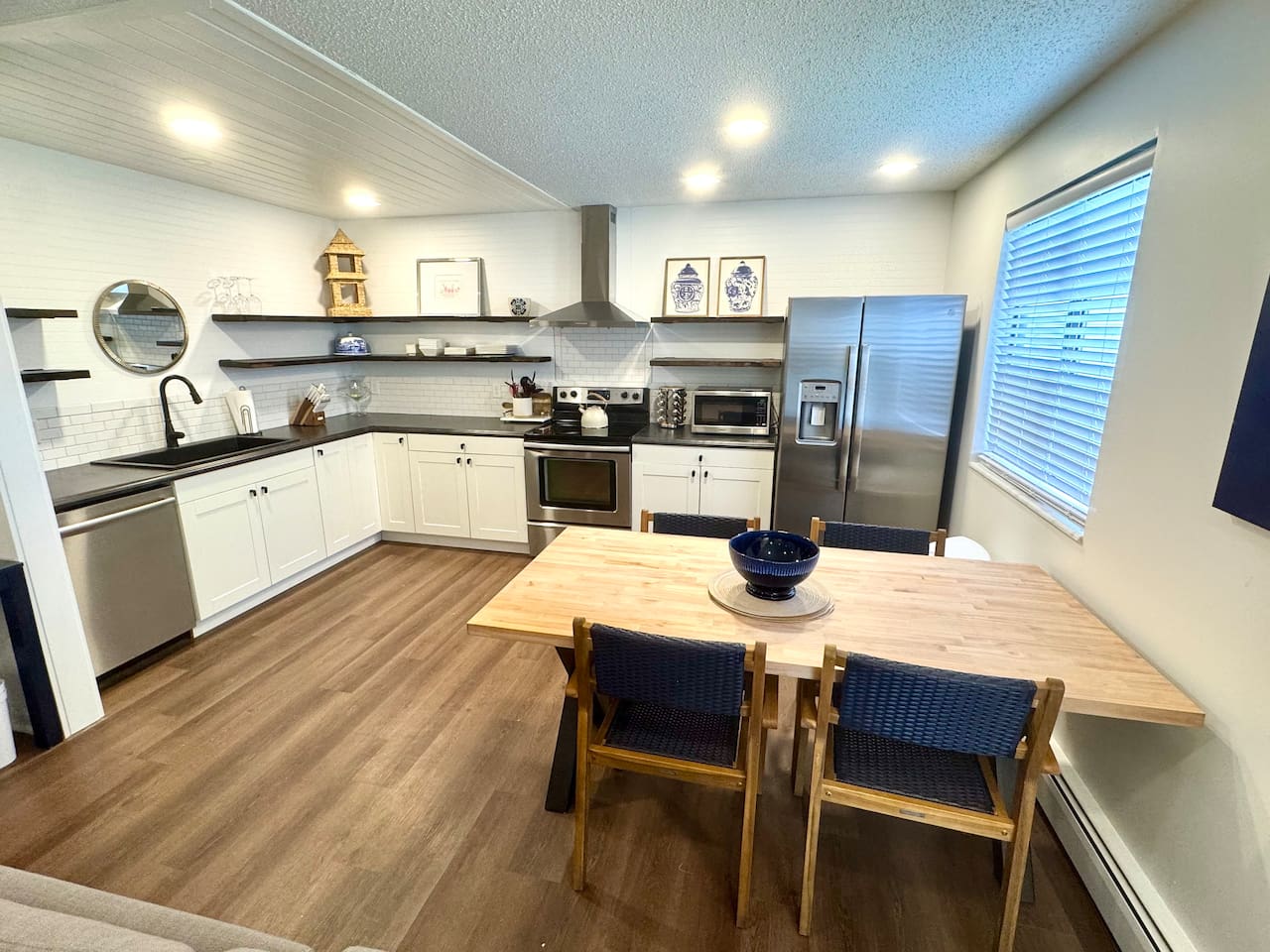 Modern kitchen with stainless steel appliances, open shelving, and a large butcher block dining table. Fully equipped for cooking, dining, and gathering. Bright, stylish, and functional—perfect for shared meals and memories