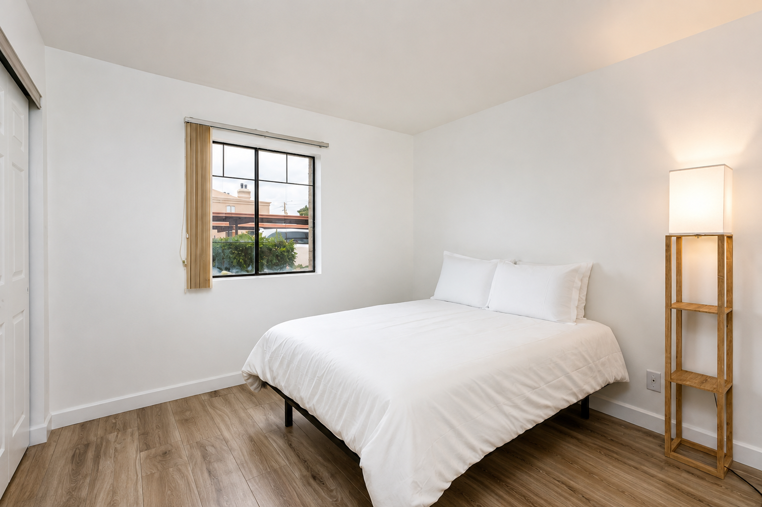Simple queen bedroom with fresh white bedding, wood-look floors, closet space, and a floor lamp by the bed.