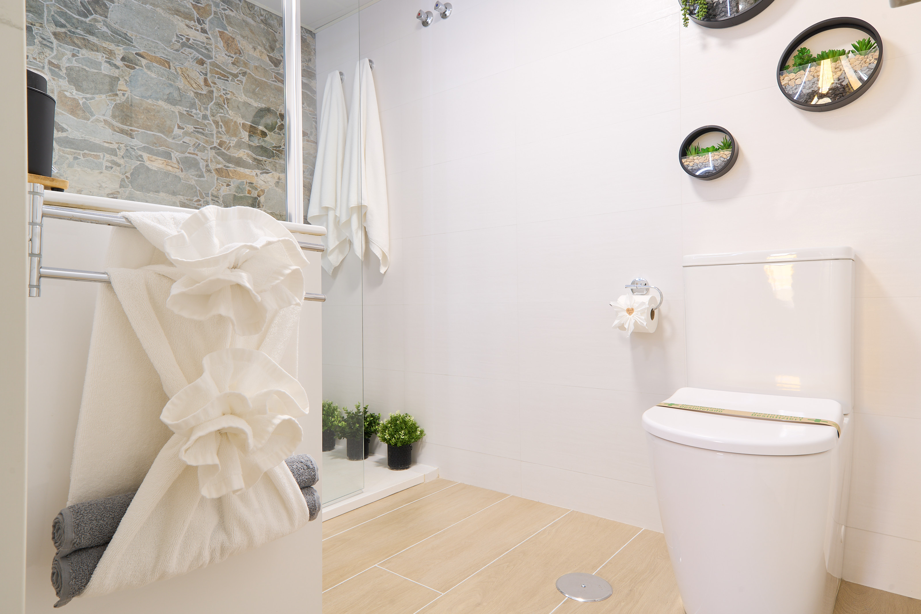 Modern bathroom with walk-in rain shower, stone accent wall, LED mirror, and fresh spa-like touches for your comfort.
