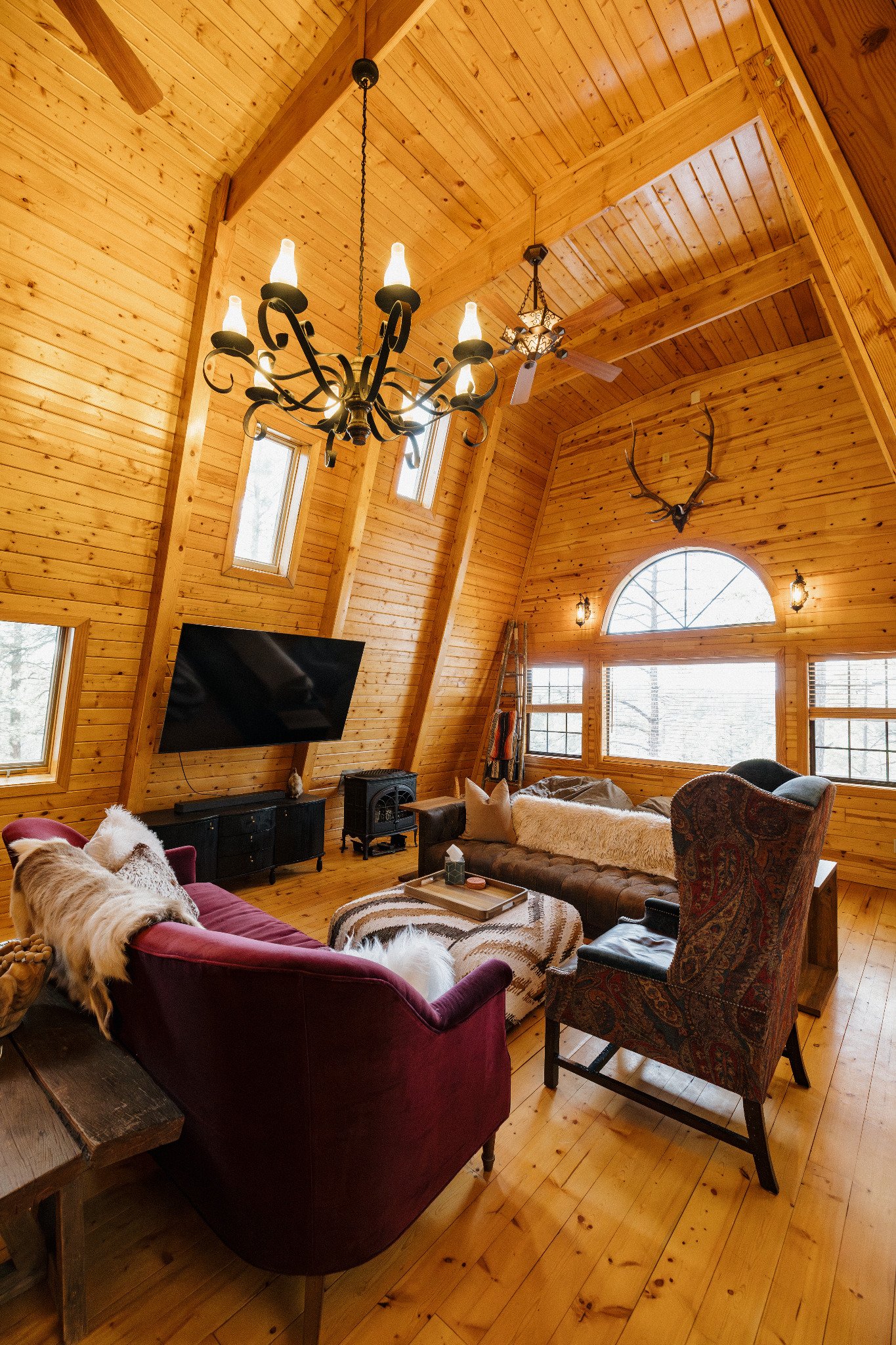 Light-filled A-frame living room with vaulted wood ceilings, eclectic seating, and cozy gathering spaces—perfect for lounging, game nights, and slow mornings in a warm, character-filled White Mountains cabin.