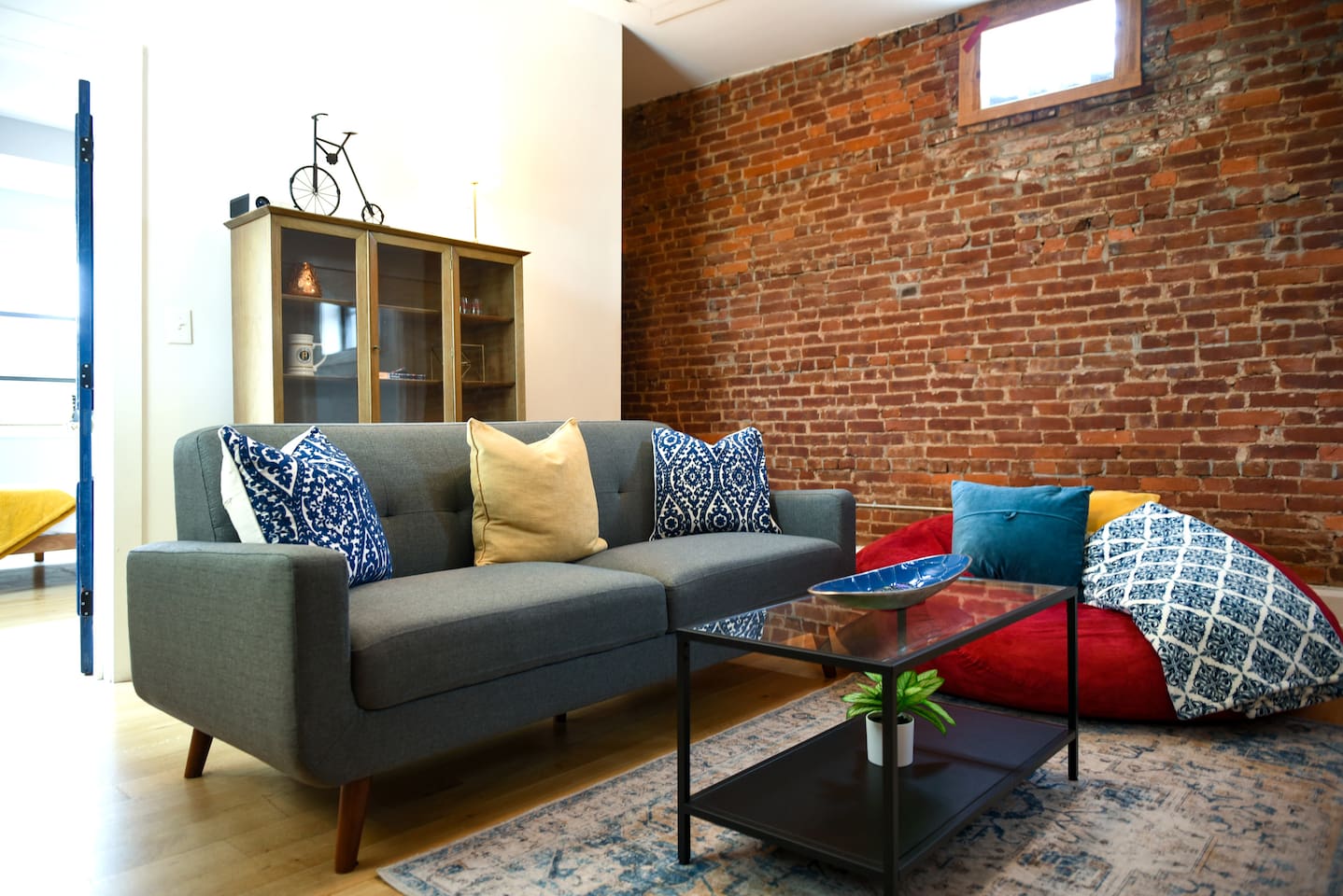 This living room features a projector screen, comfy couch, and a chic brick wall—plus a cozy rug and bean bag for the perfect movie night or chill session.