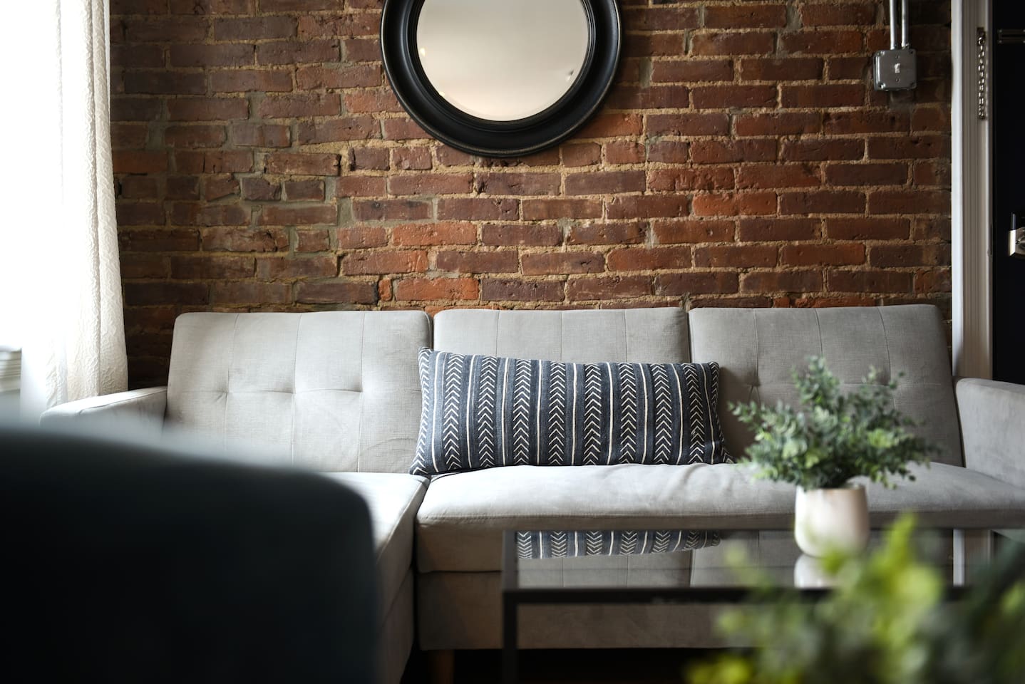 Lounge in a tastefully designed living room with a brick accent wall, large windows, and a mix of chic furniture for the ultimate cozy yet refined vibe.
