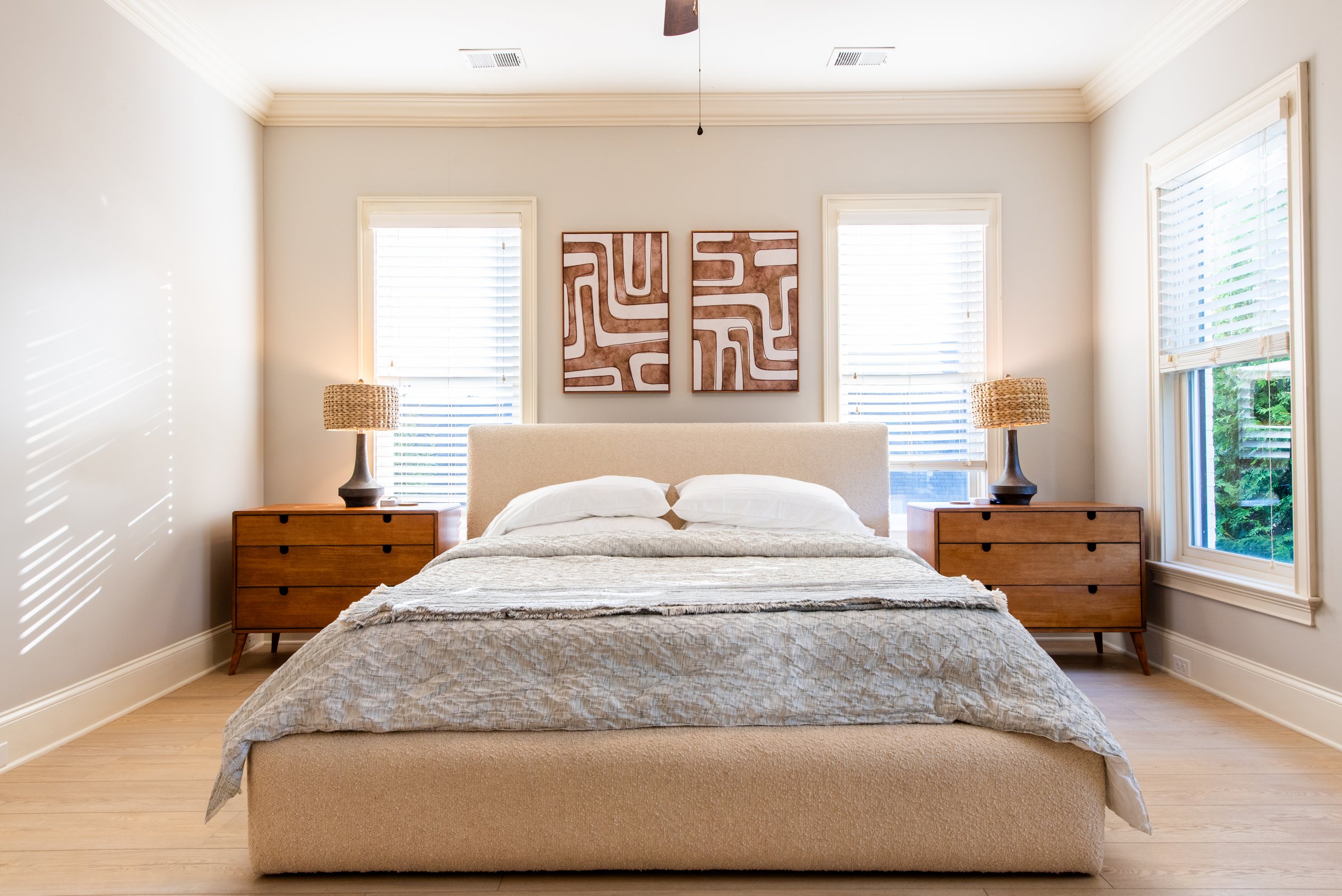 The primary suite features a plush upholstered bed and large windows.