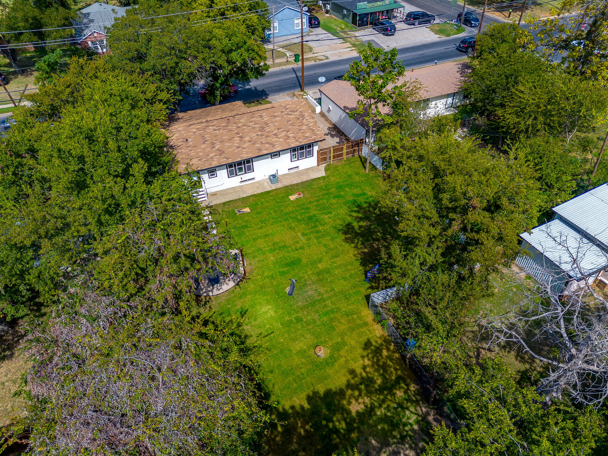 Aerial view of fenced backyard, trees, and play space for kids or pets