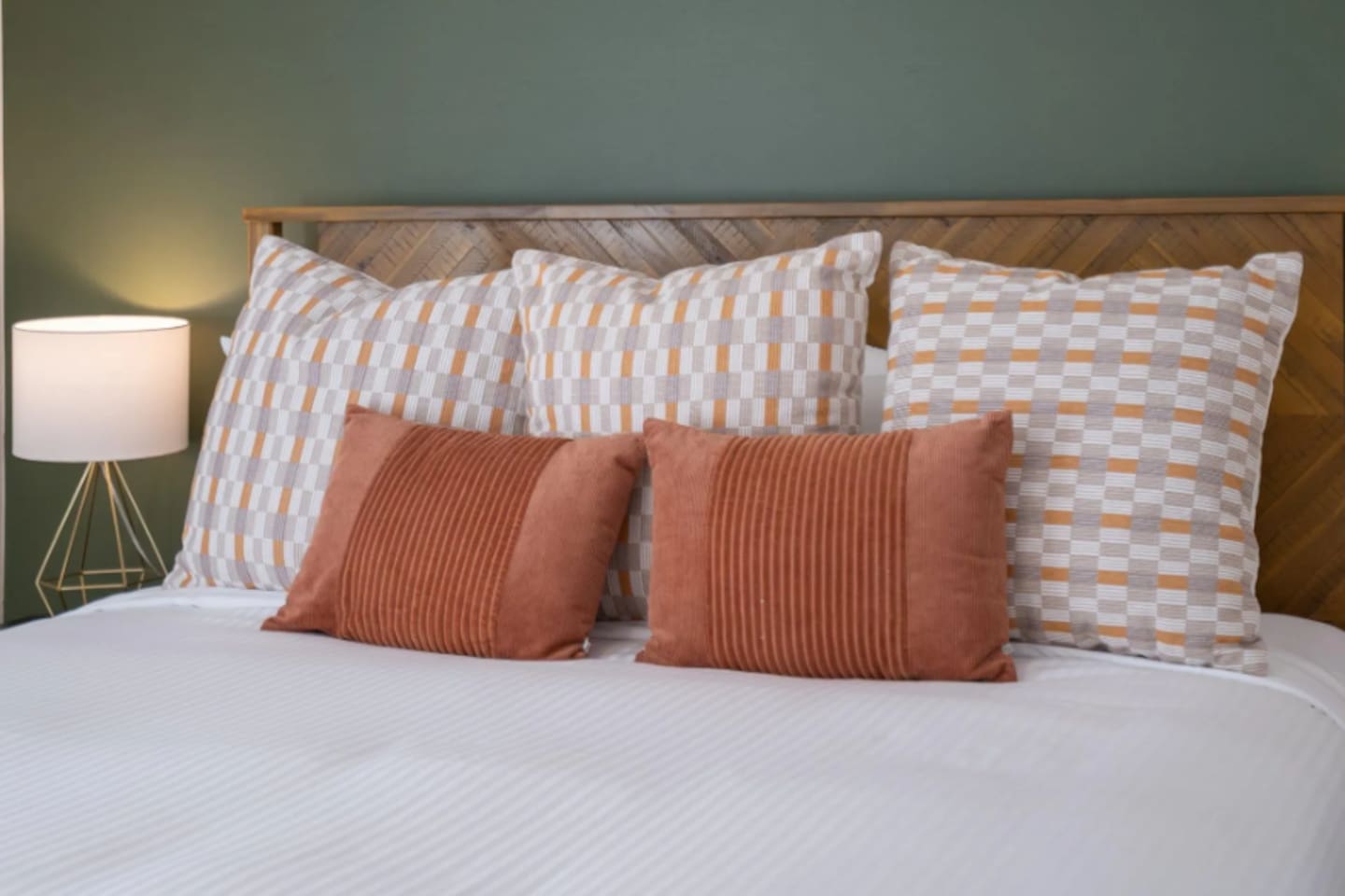 Layered pillows in warm rust and neutral patterns turn simple white bedding into something that feels curated and cozy.
