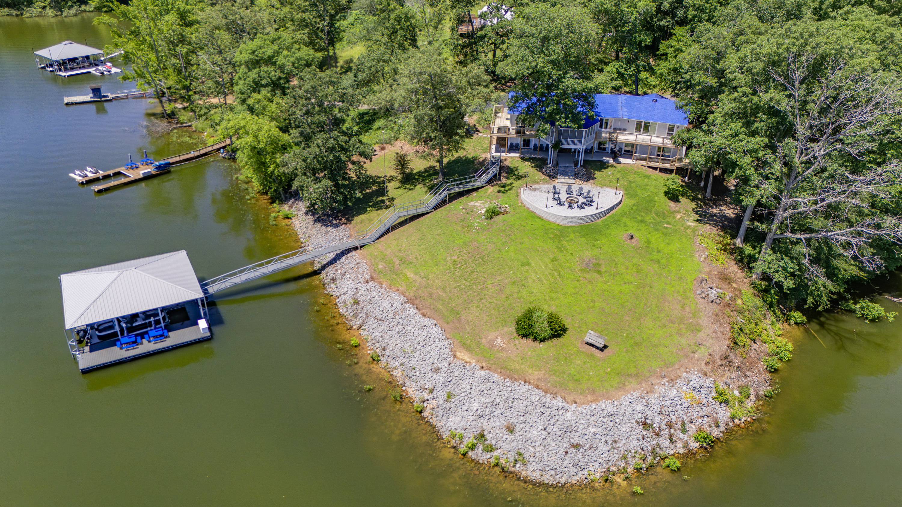 This overhead view shows the full lakefront layout, including the house, firepit area, lawn, shoreline, and dock.
