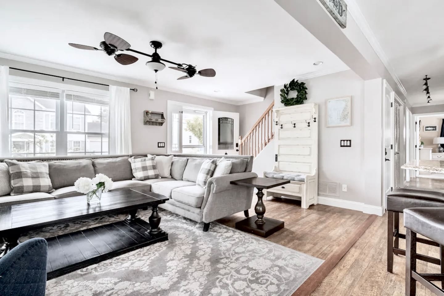 This open-concept living area offers a plush sectional, a unique multi-blade ceiling fan, and beautiful hardwood floors. A convenient hall tree with a bench and hooks sits near the stairs for easy gear storage during your stay.