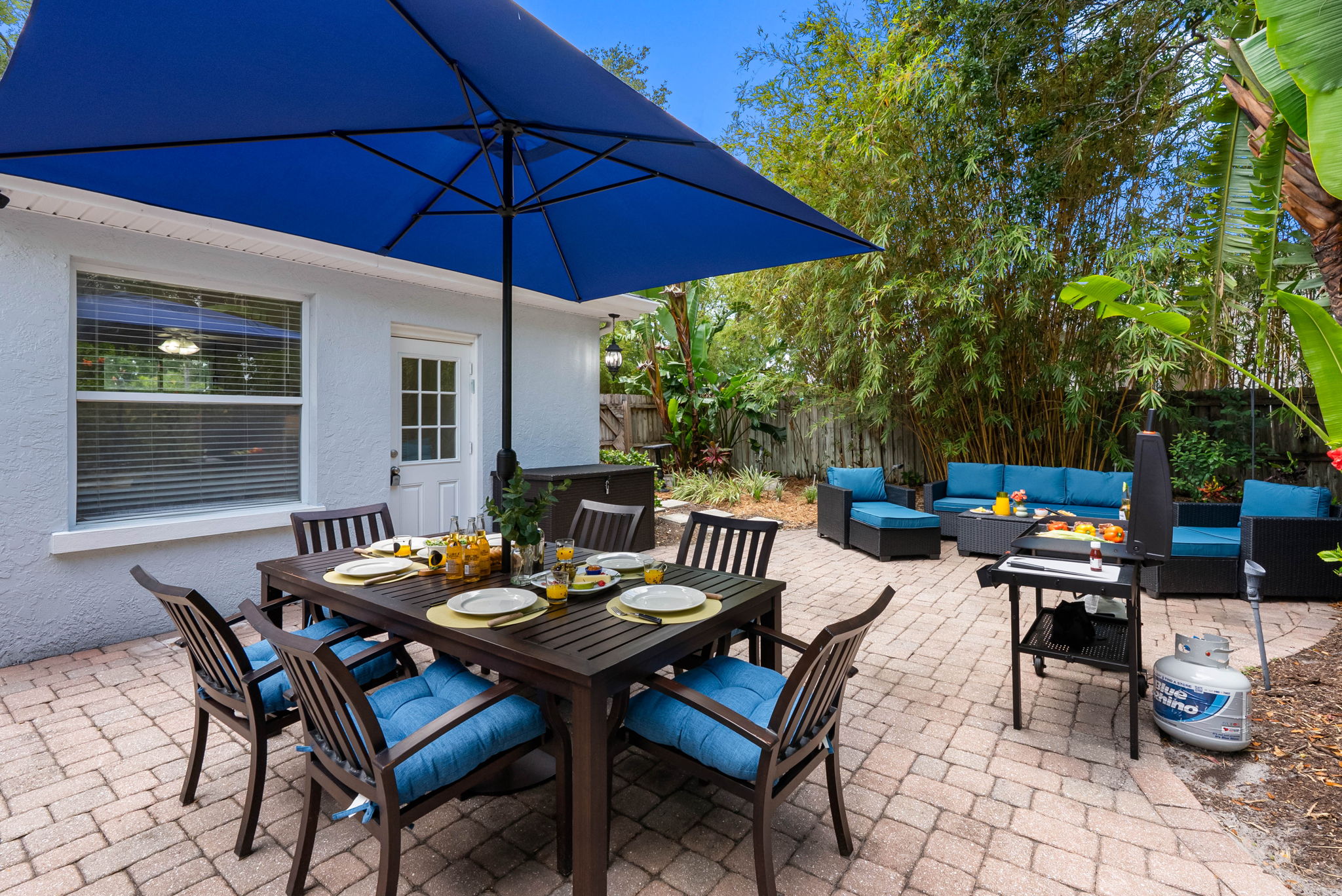 Lush greenery lines the patio, including banana leaves, hibiscus plants, bamboo, and palms, giving the entire space a secluded, garden-like feel.