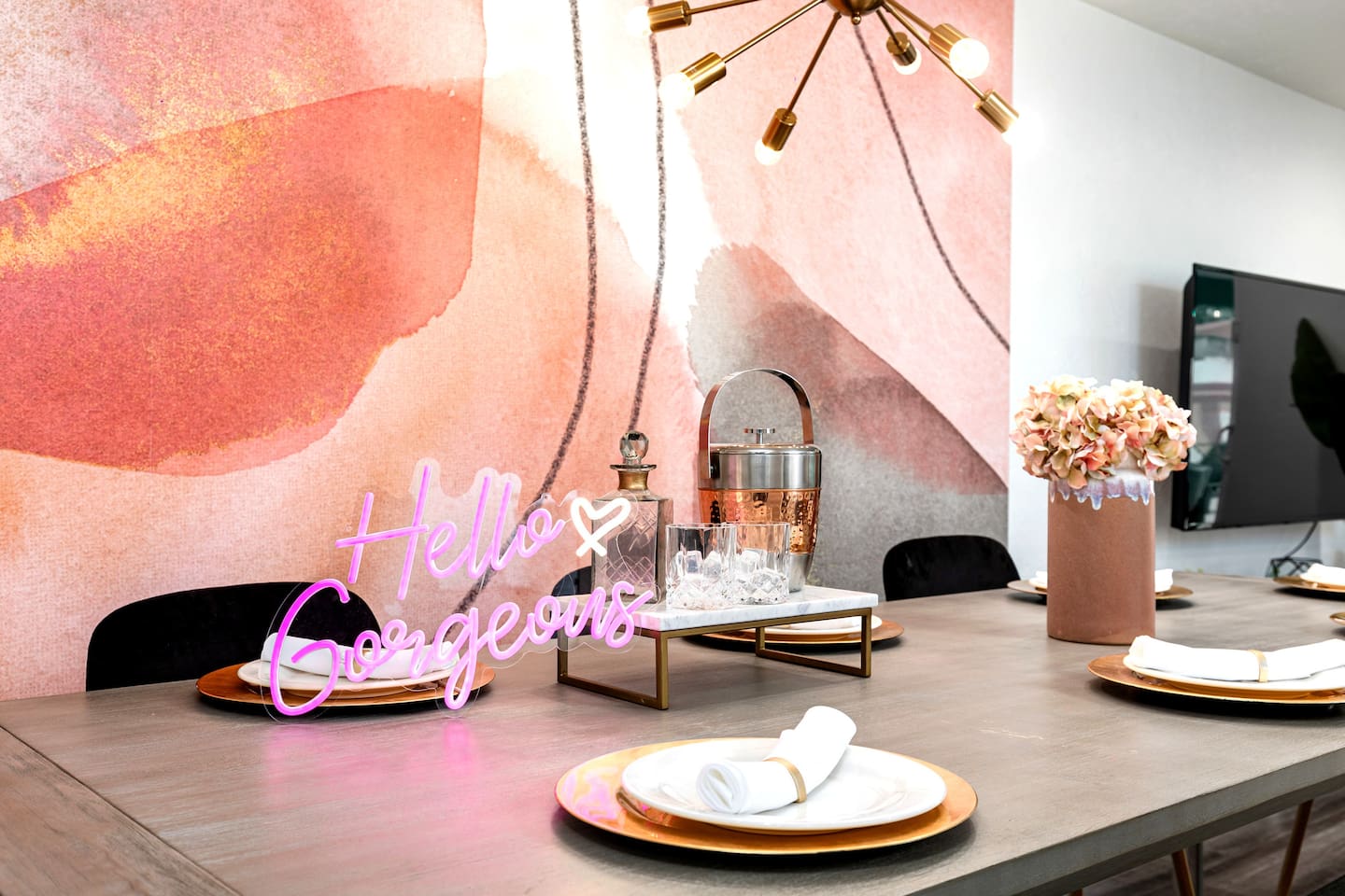 The “Hello Gorgeous” neon sign and stylish bar tray setup bring personality and charm to this modern gathering space.

