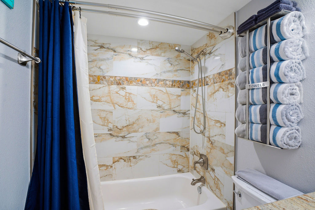 Spa-like bathtub and shower combo with elegant tile surround, plush towels, and bright modern lighting.