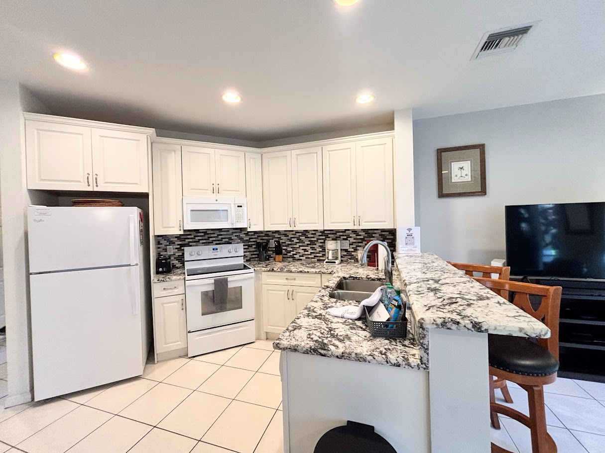 Updated kitchen featuring granite countertops, full-size appliances, breakfast bar seating, and an open view into the living area.