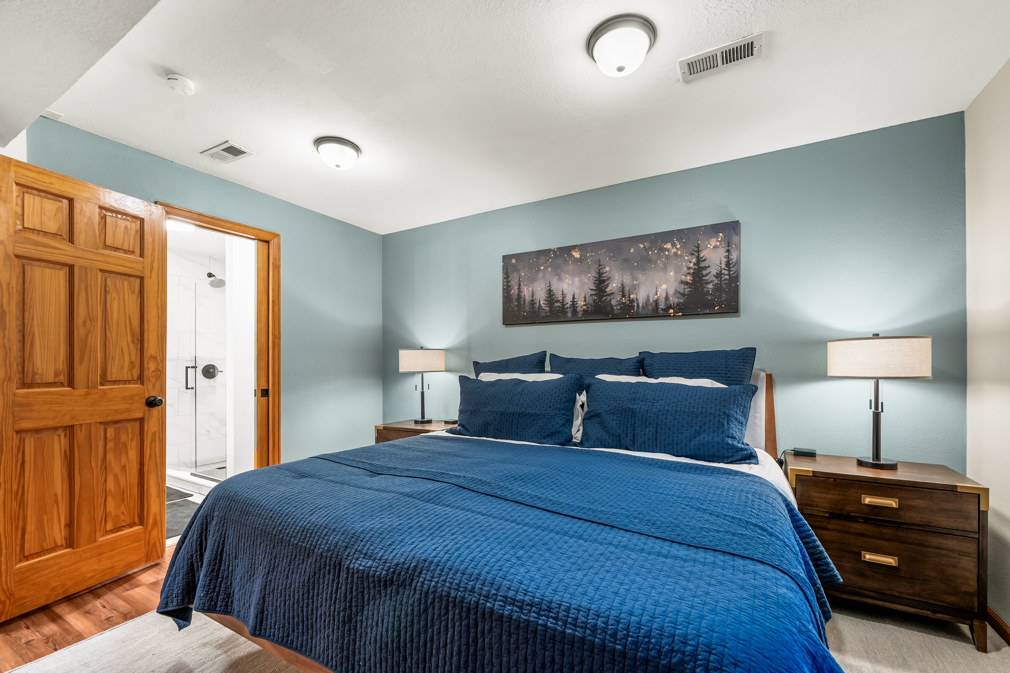 🛏️✨ Cozy bedroom with a plush king-sized bed, soft lighting, and calming mountain decor—plus easy access to the sleek bathroom 🚿 for a relaxed start to your day. 