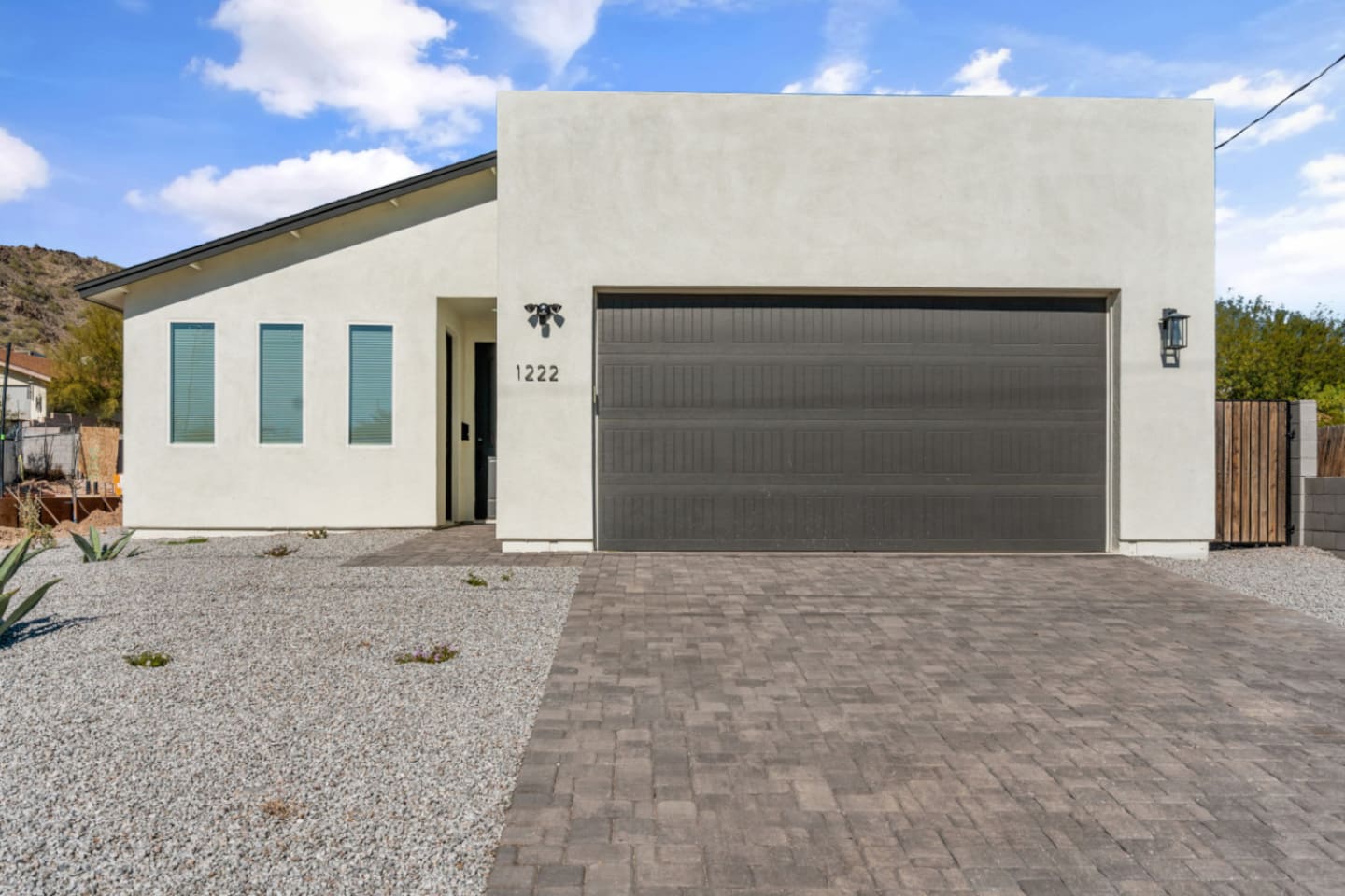 Modern front exterior with garage access, paved driveway, and simple desert landscaping.