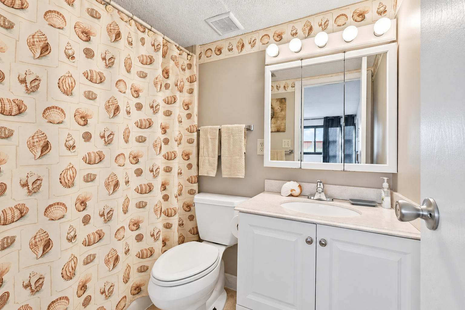 Ensuite bathroom with shell-pattern shower curtain, white vanity storage, and beach-themed details.