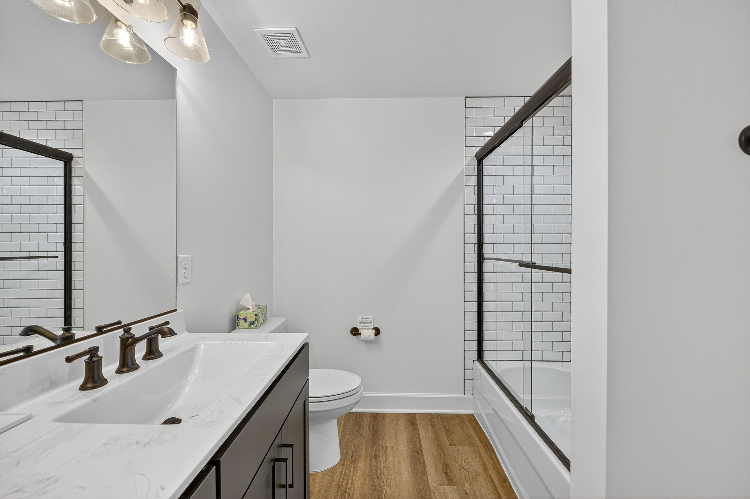 Impeccably designed full bath with a spacious double vanity, warm wood-grain flooring, and a classic subway-tiled shower/tub combination.