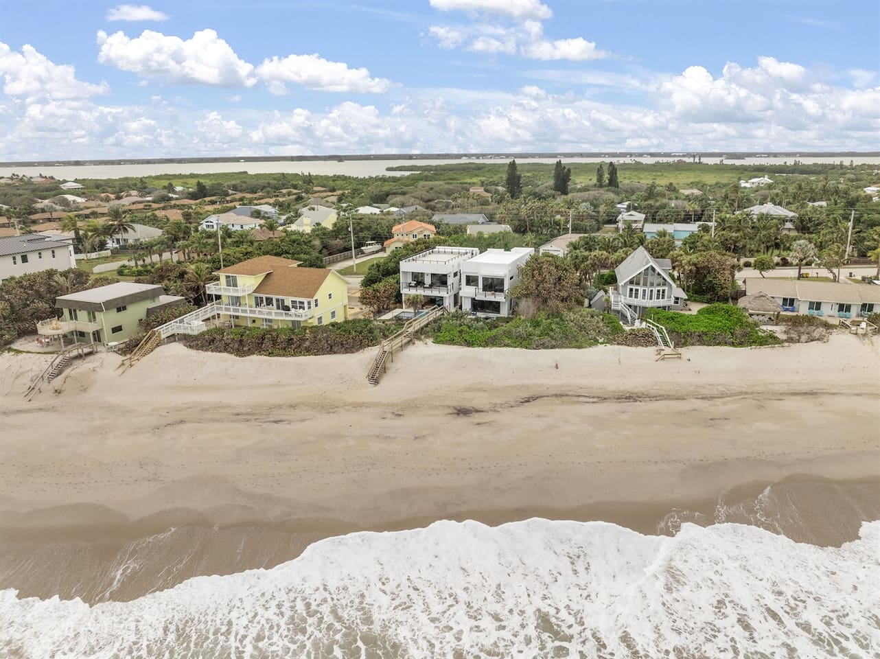 This breathtaking backyard showcases the neighborhood, vibrant trees, the shimmering sea, soft white sand, and fluffy white clouds, offering a perfect blend of coastal beauty and natural serenity.