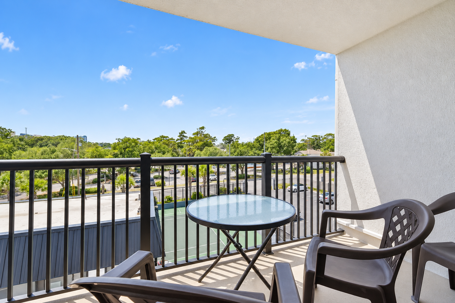 Covered balcony with table seating, chairs, and a treetop view over the Holiday Towers area.