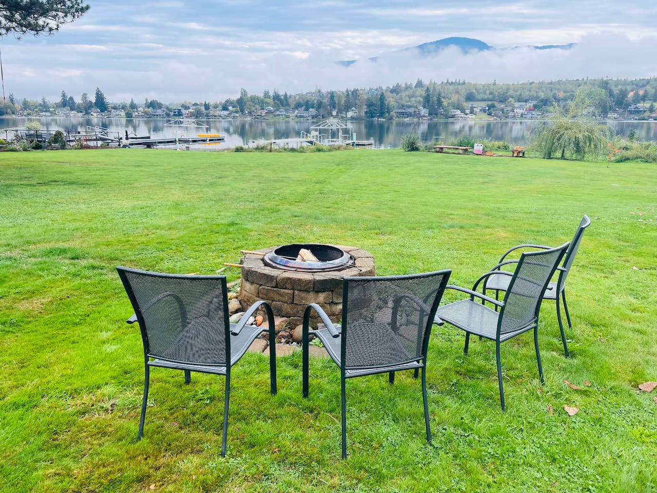An expansive grassy backyard leads to the lake, where a dock and fire pit invite evenings outdoors. The open lawn is perfect for relaxing or playing, while the shoreline and gentle water create a peaceful connection between land and lake.