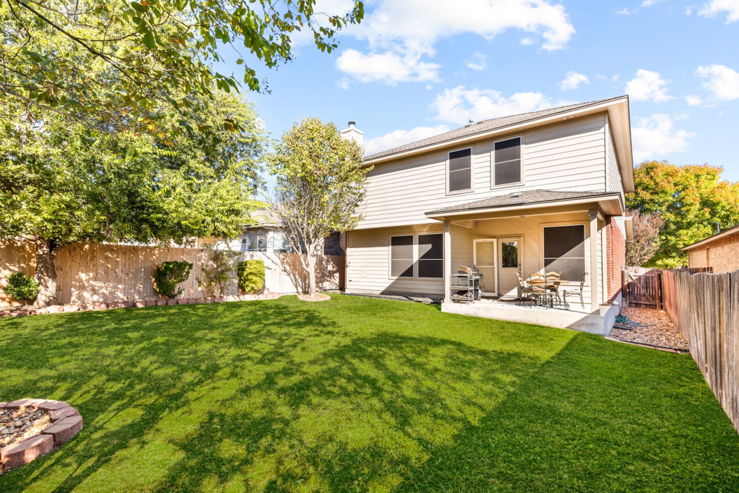 Spacious fenced backyard with BBQ gas grill, outdoor dining, and furniture for family cookouts or gatherings.