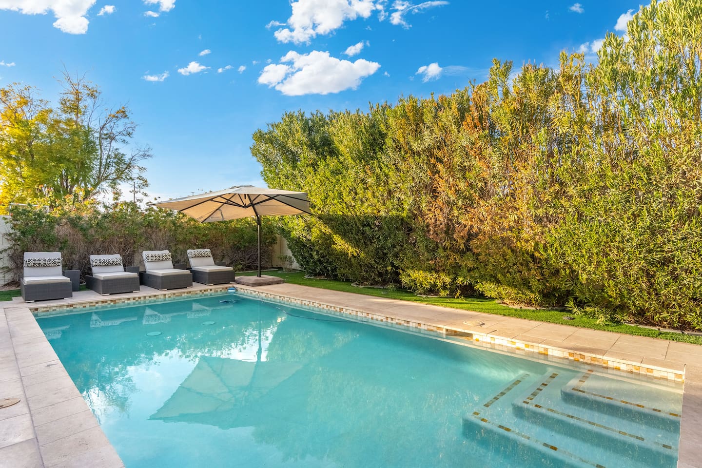 Comfortable sun loungers line the pool's edge, shaded by a wide umbrella and framed by vibrant greenery — ideal for a relaxing afternoon.