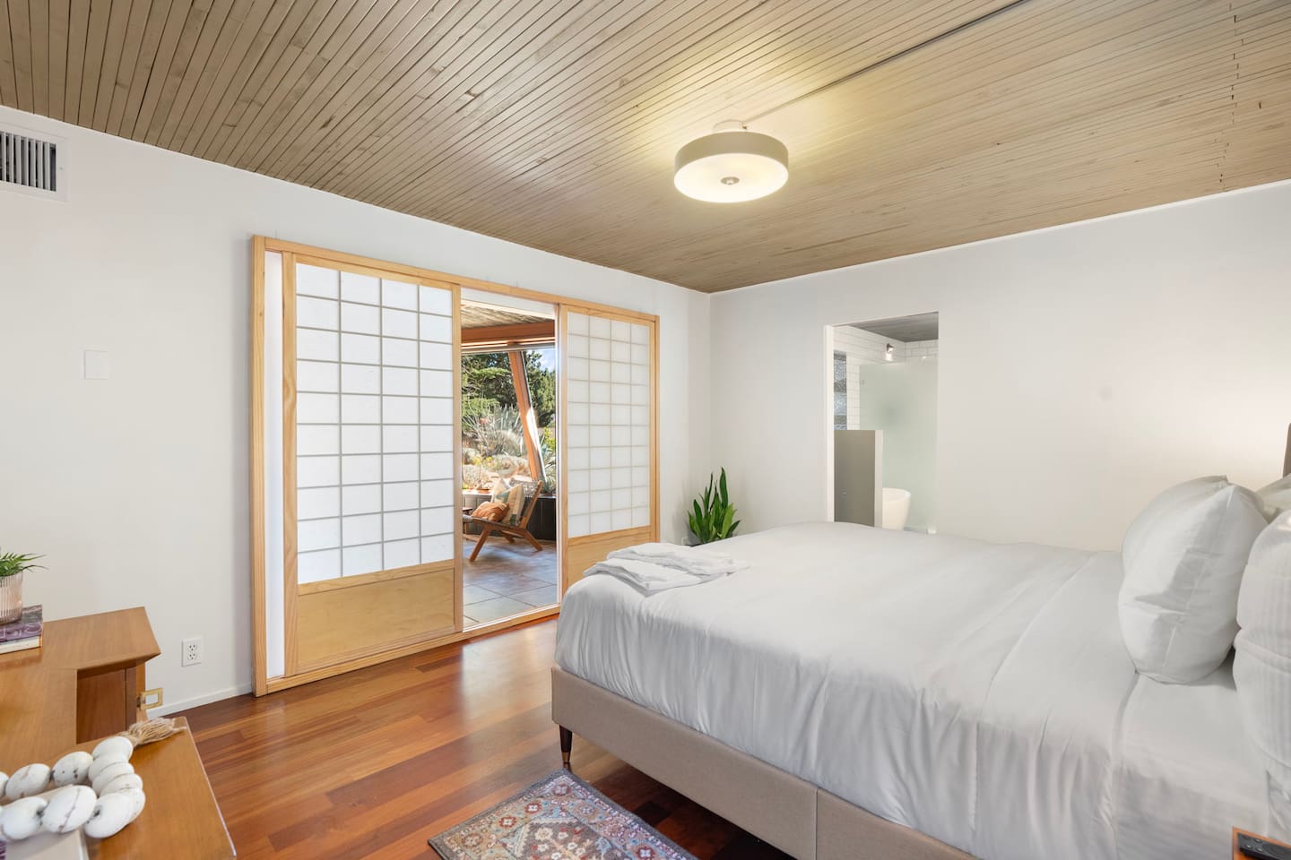 Peaceful bedroom retreat with warm wood ceilings, comfortable king bed, and sliding shoji-style doors that open to a bright sitting area and ensuite bath.