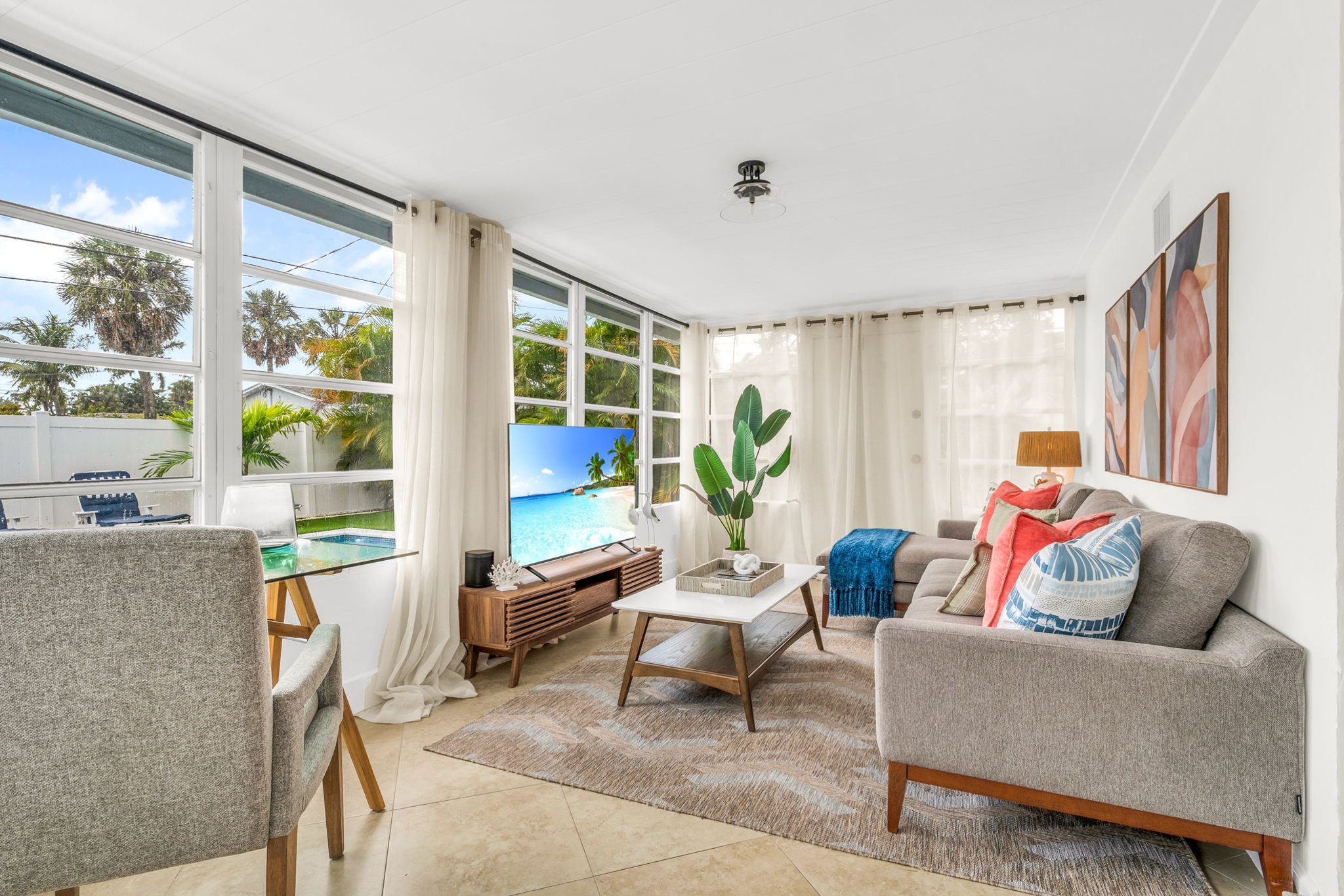 A beautifully designed Florida sunroom with wrap-around windows, modern furnishings, a Smart Fire streaming TV, and tranquil pool views—ideal for lounging, morning coffee, or working in style.