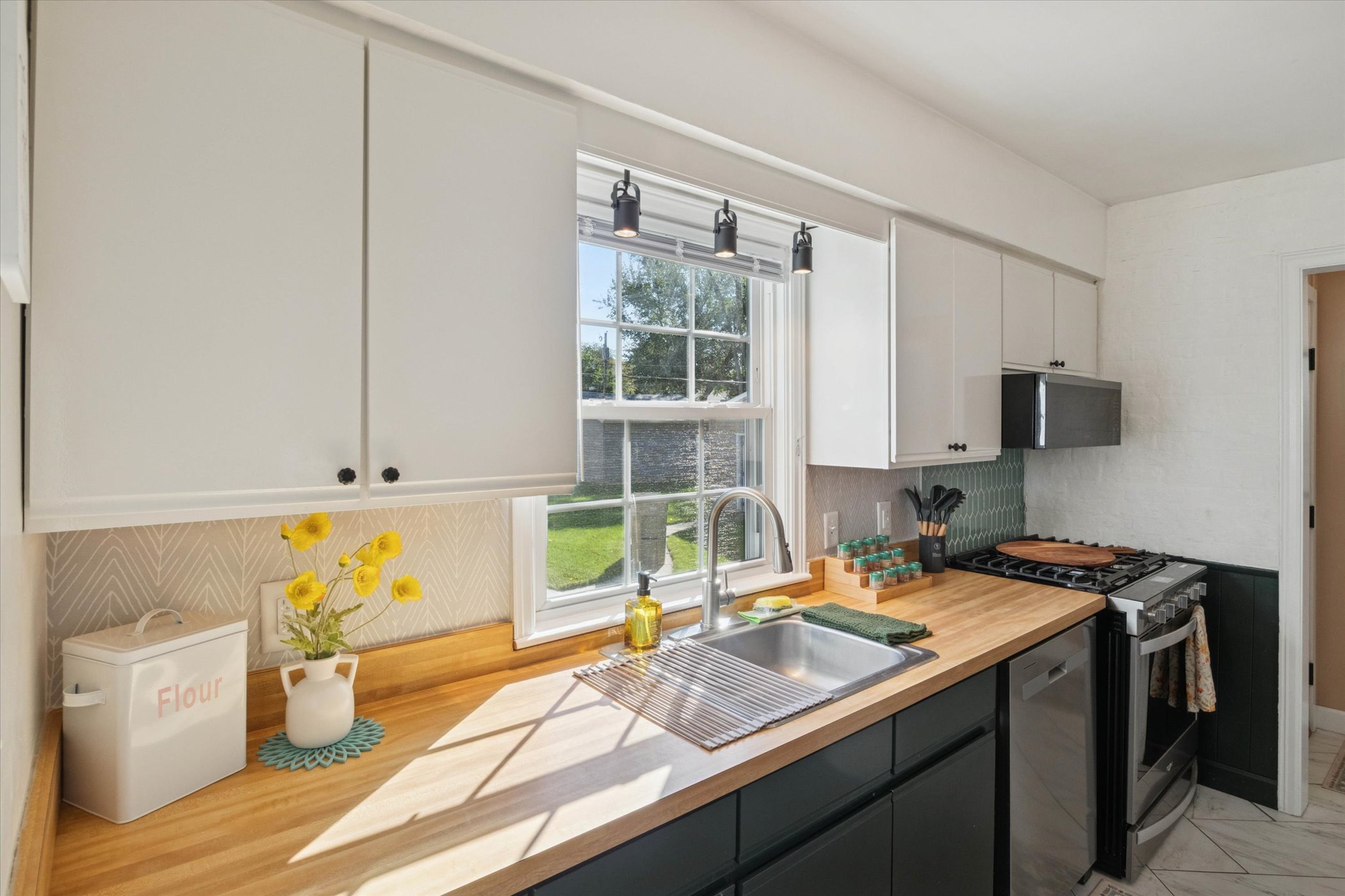 Sunlight warms the counter in our South Bend kitchen, where new stainless Whirlpool smart appliances, spices, utensils, and flour are stocked for alfresco pizza nights near Notre Dame.