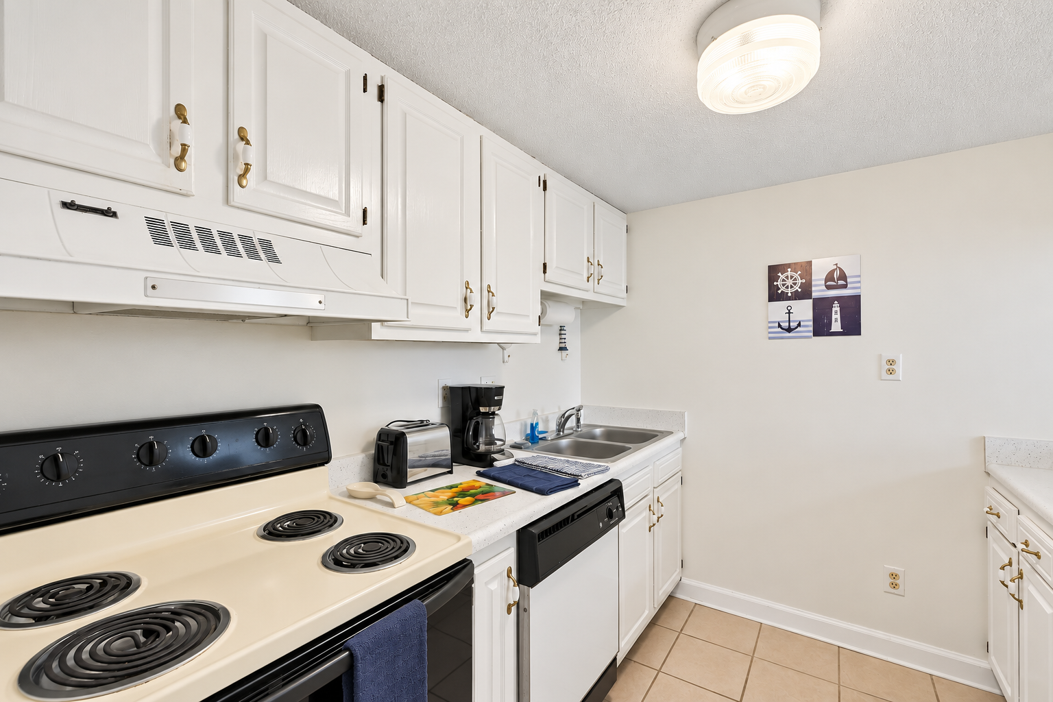 Kitchen with electric stove, dishwasher, coffee maker, toaster, and white cabinet storage for easy meals.