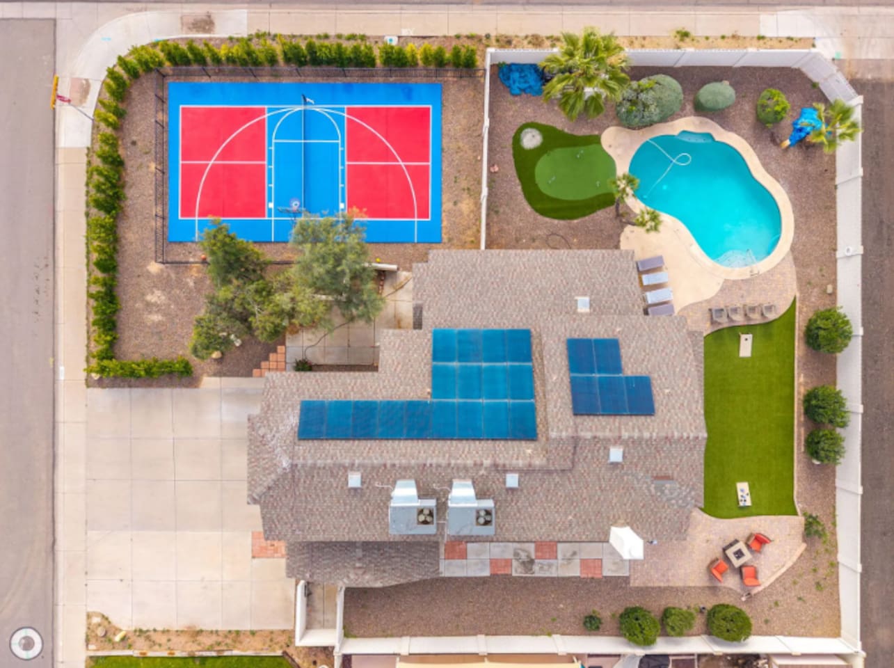 Aerial view of resort-style compound with basketball court, resort pool, solar panels, and sprawling grounds.