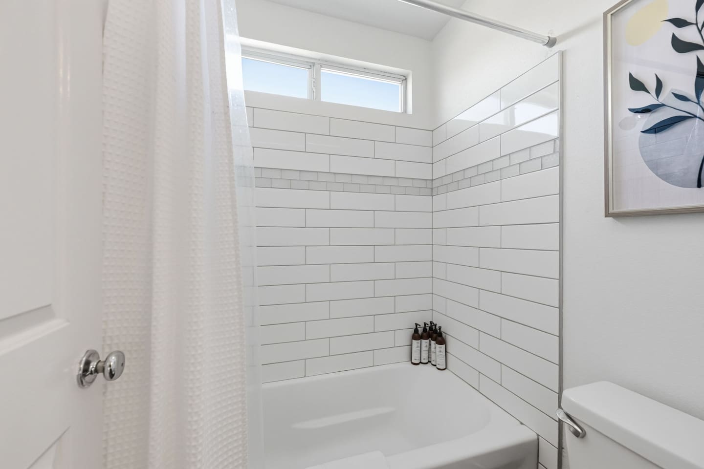 Shower + Bath Tub combo with tile surround and natural light. Three full bathrooms total — each stocked with Ginger Lily Farms bath essentials.
