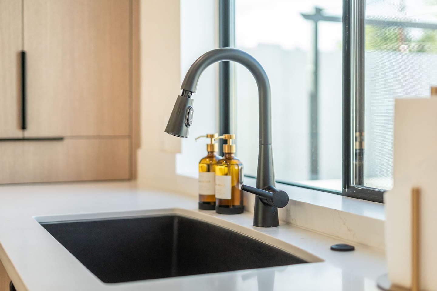 Sleek black faucet and deep sink with backyard views.