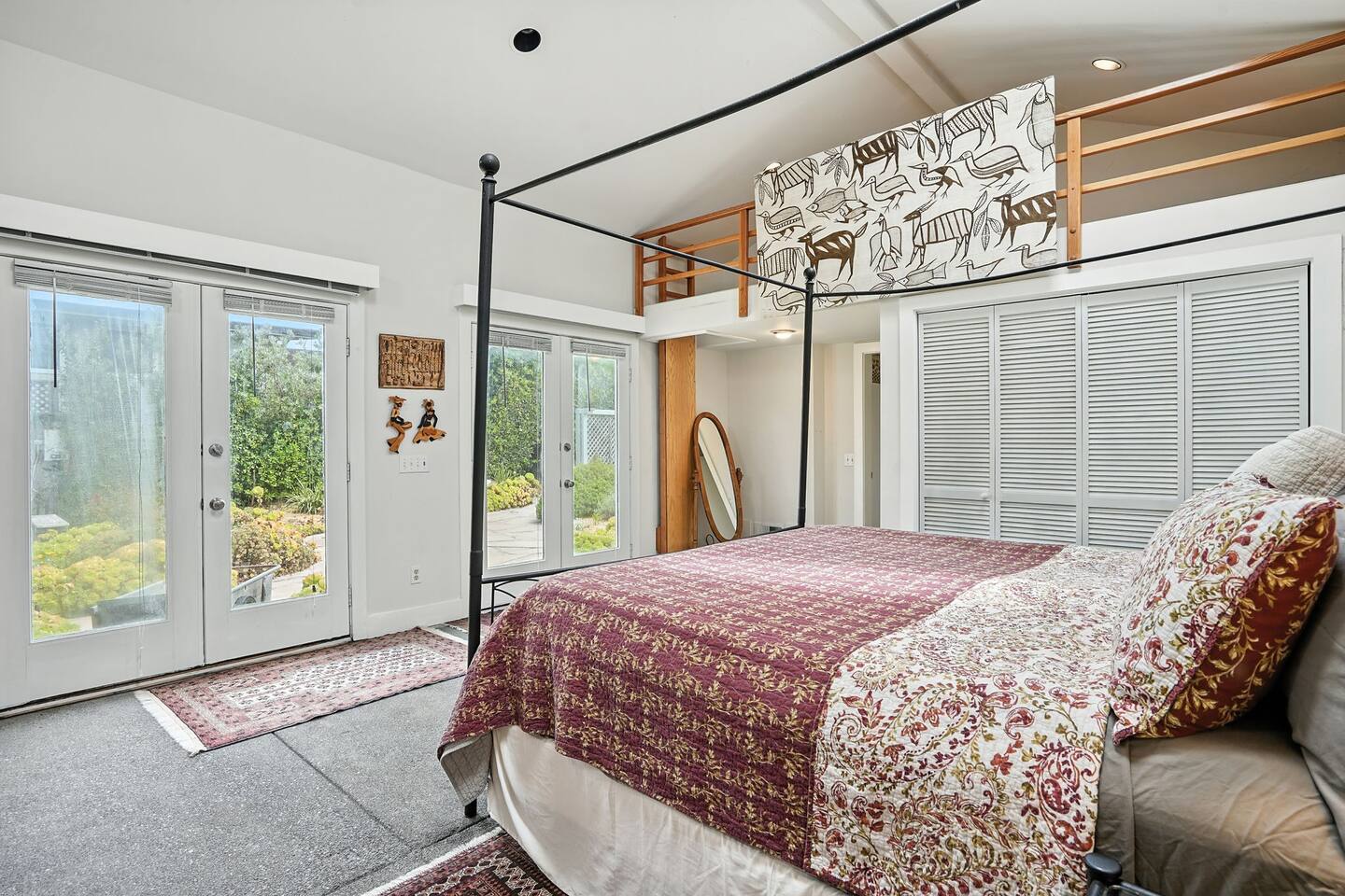 - Spacious bedroom with four poster bed, patterned bedding, and loft space above for extra charm  
- Double glass doors open to a private patio with garden views  
- Neutral tones and natural light create a warm, inviting retreat