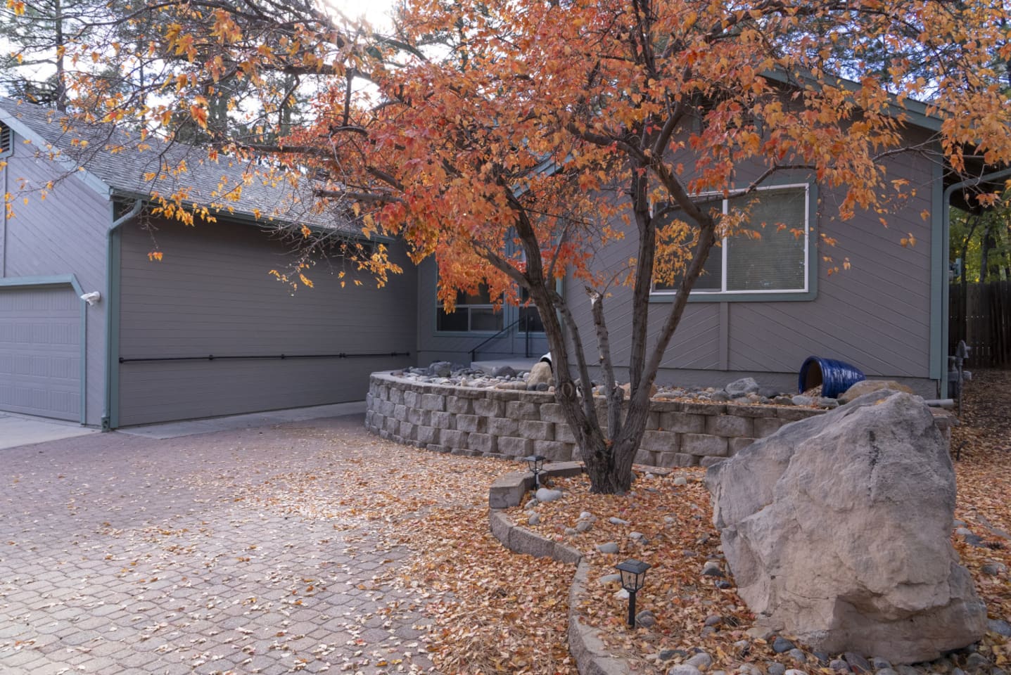 Home entrance with paved courtyard, mature trees, and natural stone details.