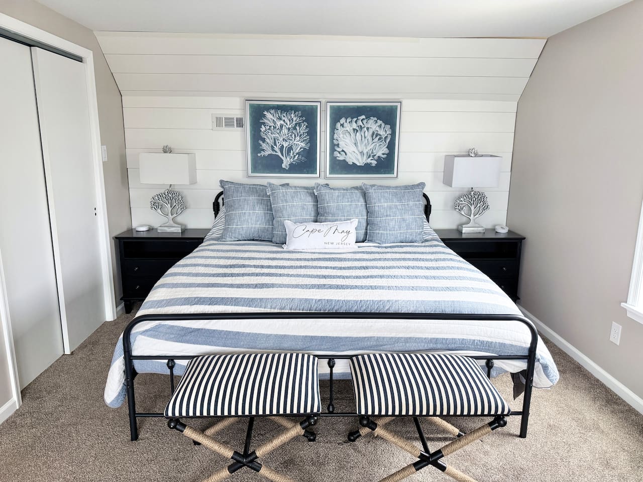 Discover a serene bedroom retreat designed with a calm, coastal aesthetic. The space features a cozy bed adorned with blue and white accents, framed by a charming shiplap wall, making it an ideal, restful sanctuary for your vacation.