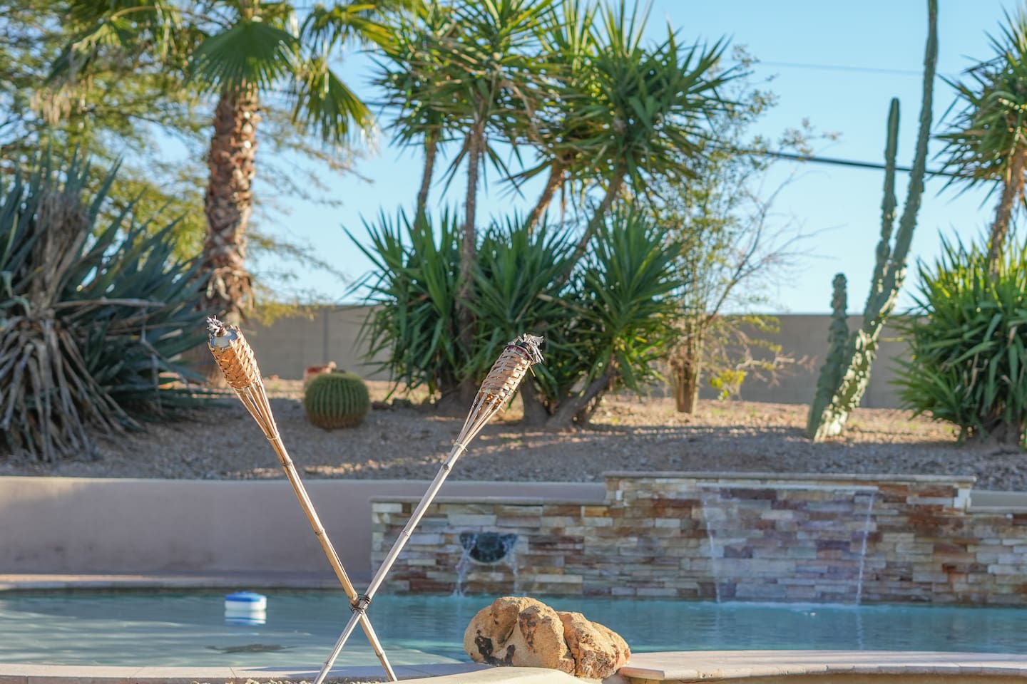 Peaceful poolside details with tiki torches, water features, and lush desert greenery.