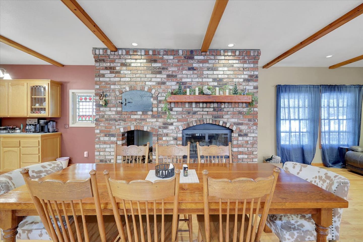 Dining area with large table seating, brick fireplace backdrop, and warm cabin-style details for shared meals.