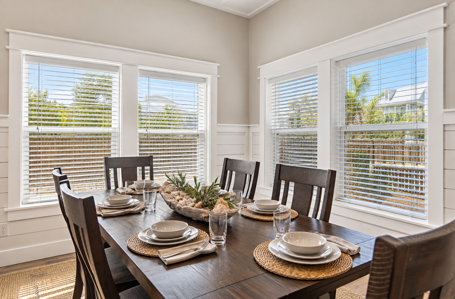 Bright, inviting dining area with a spacious table set for six, surrounded by natural light, coastal inspired details, and a comfortable open concept living space.