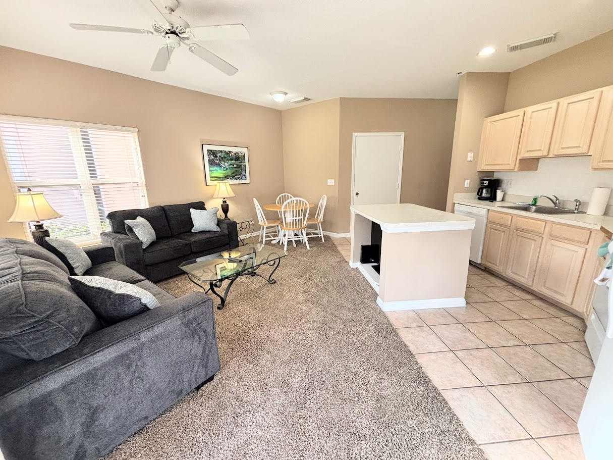 Open-concept living, dining, and kitchen area with comfortable seating, tile and carpet flooring, and a bright, functional layout.