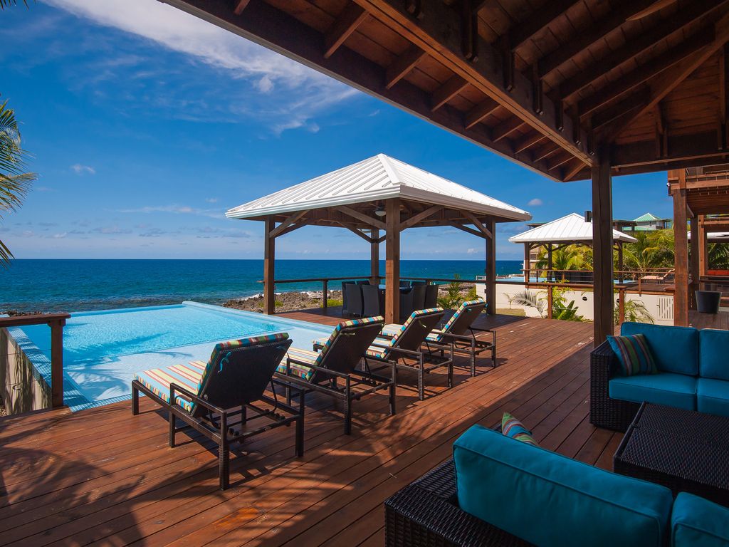 Where the walls disappear. The South House Great Room features massive accordion glass doors that open entirely to the iron shore, letting the Caribbean breeze and the sound of the waves become part of your living space.