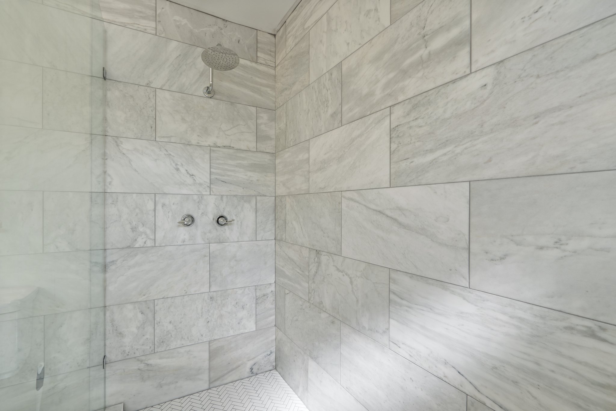Bathroom 1 oversized walk-in rain shower with marble-style tile surround and hotel-quality finishes. Ginger Lily Farms toiletries, fresh towels, and hairdryer provided. Main house, first floor.