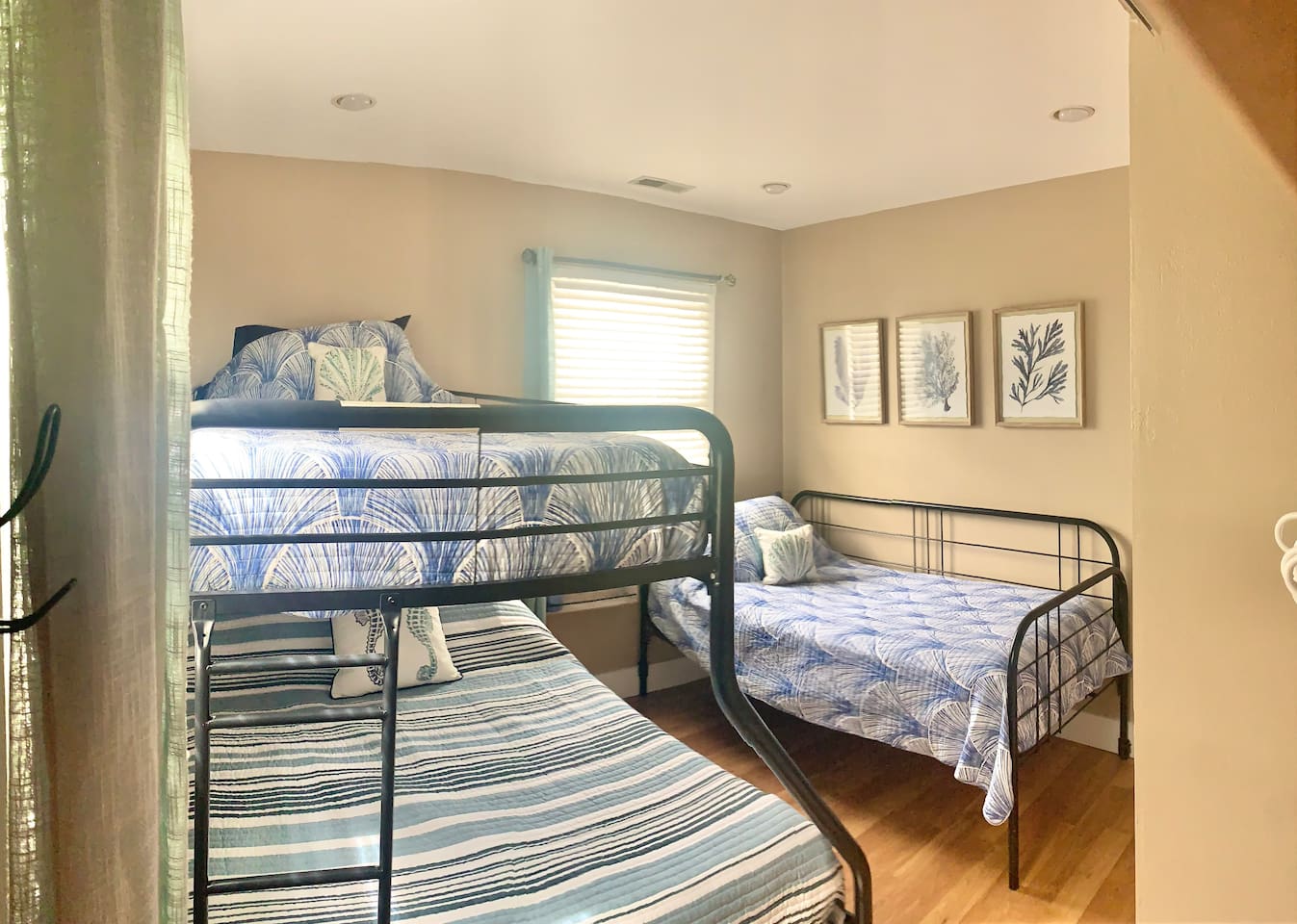 This bright bedroom features a sturdy metal bunk bed and a separate twin bed with coastal-themed linens. The well-appointed area includes charming coral artwork, making it easy to enjoy a restful night before heading to the beach.