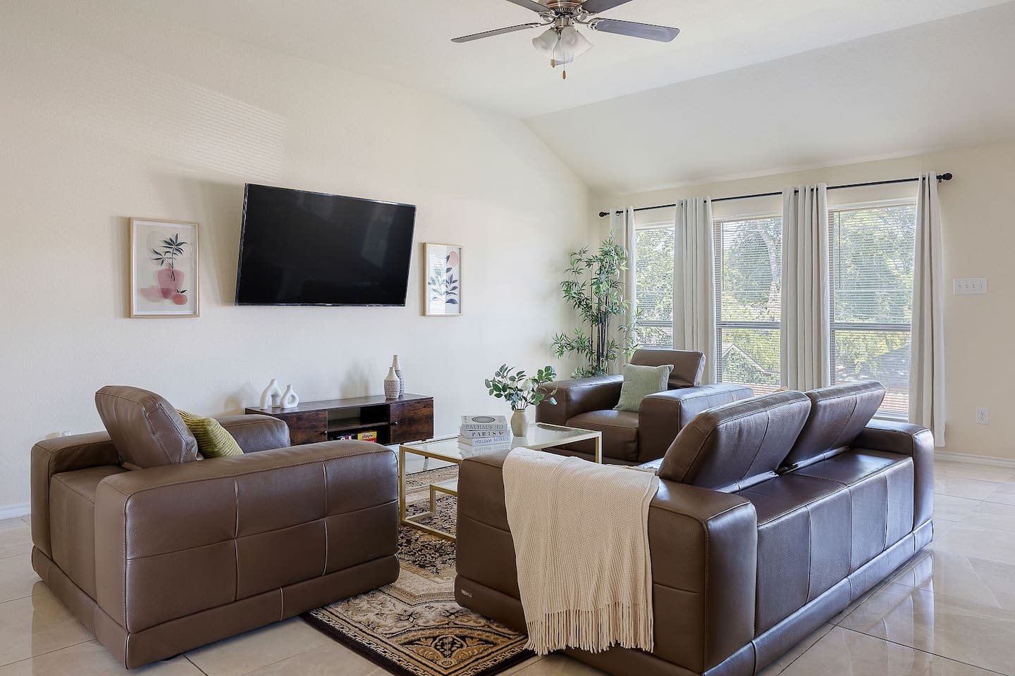 Welcome to this elegant living room with plush leather sofas and a large wall-mounted TV, bathed in natural light.