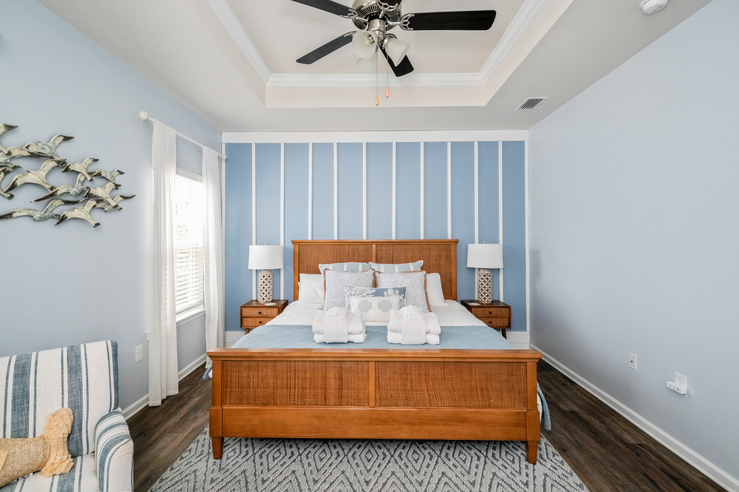 Primary Suite: Elegant King bedroom featuring an en suite bathroom, plush linens, ceiling fan, elegant bedside lamps, dresser, couch, and Smart TV.
