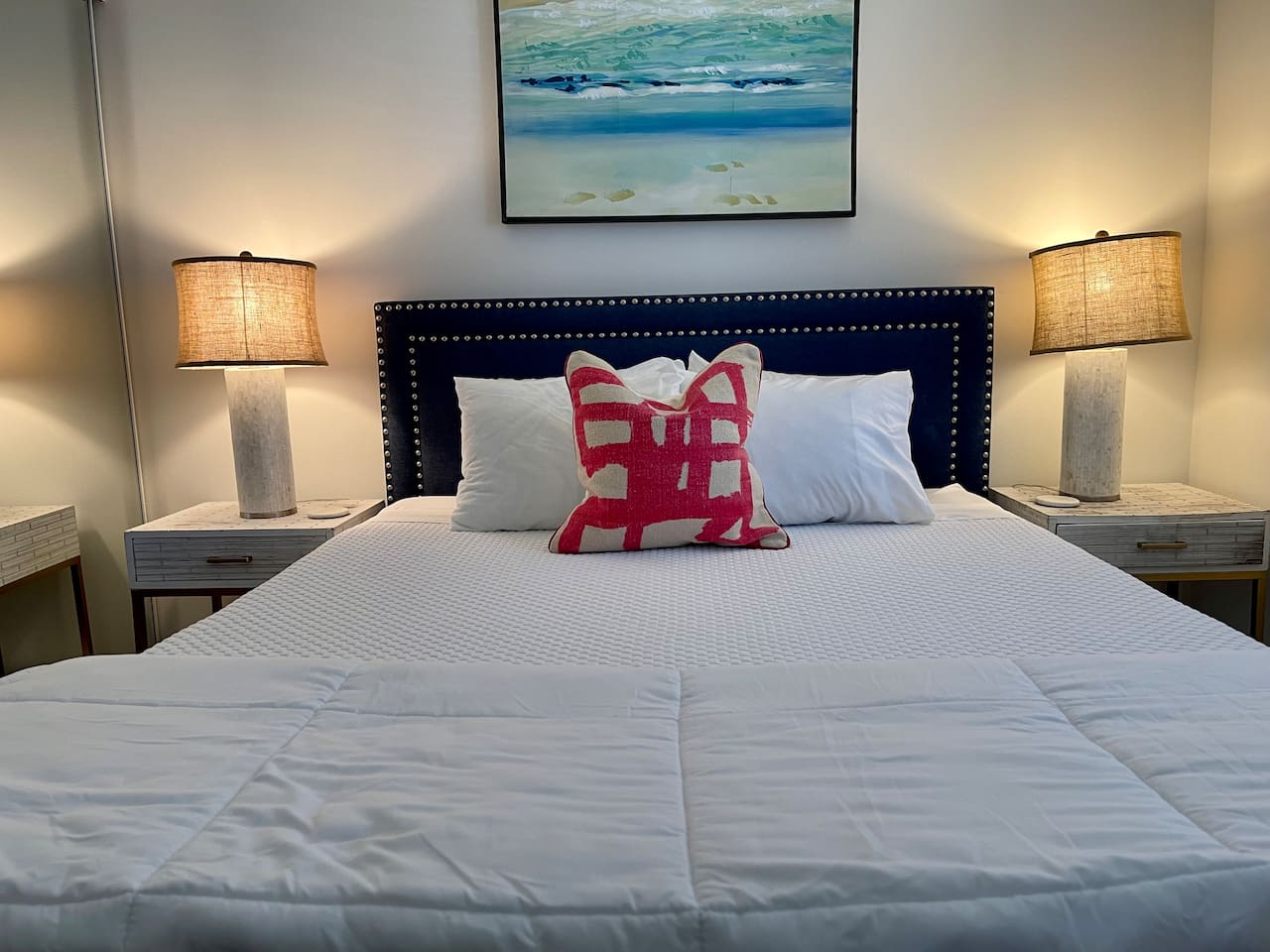 Relax in a queen bed with luxe linens, coastal art, soft lighting, and stylish modern decor.